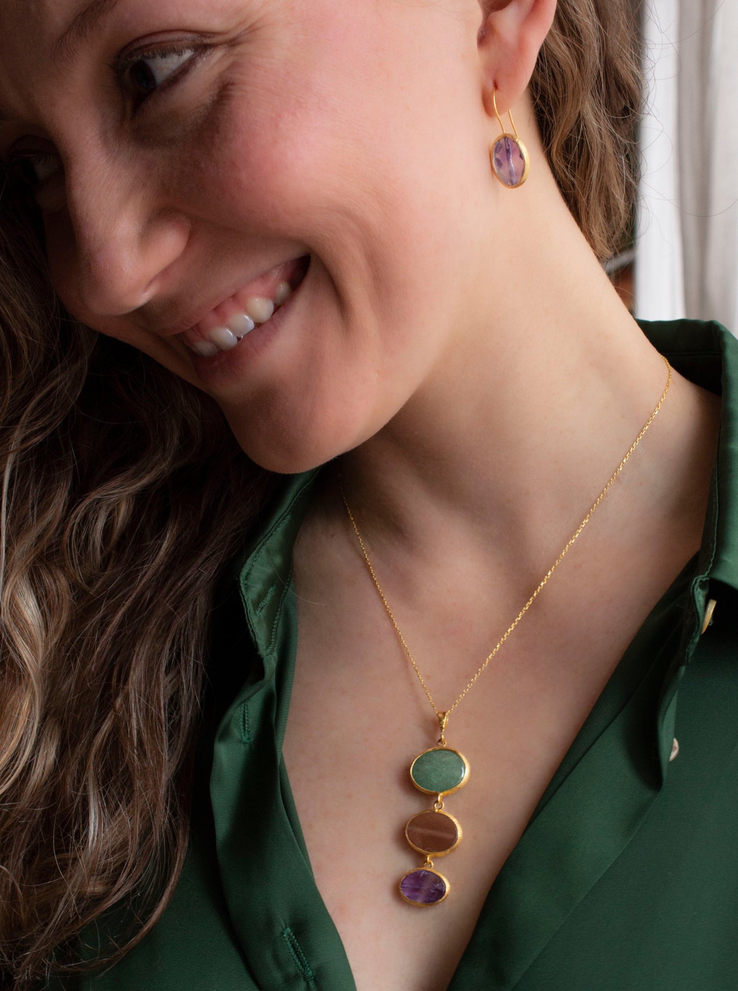 Blond curly haired woman with a green shirt wearing Charites necklace, green aventurine, pink moonstone, amethyst pendant.