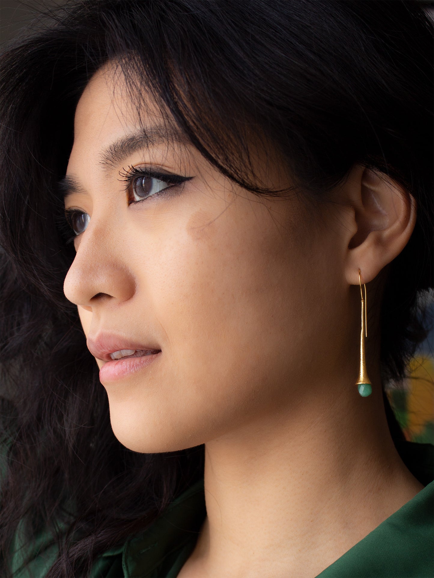 Girl wearing a long and chic gold earring with a briolette cut jade gemstone