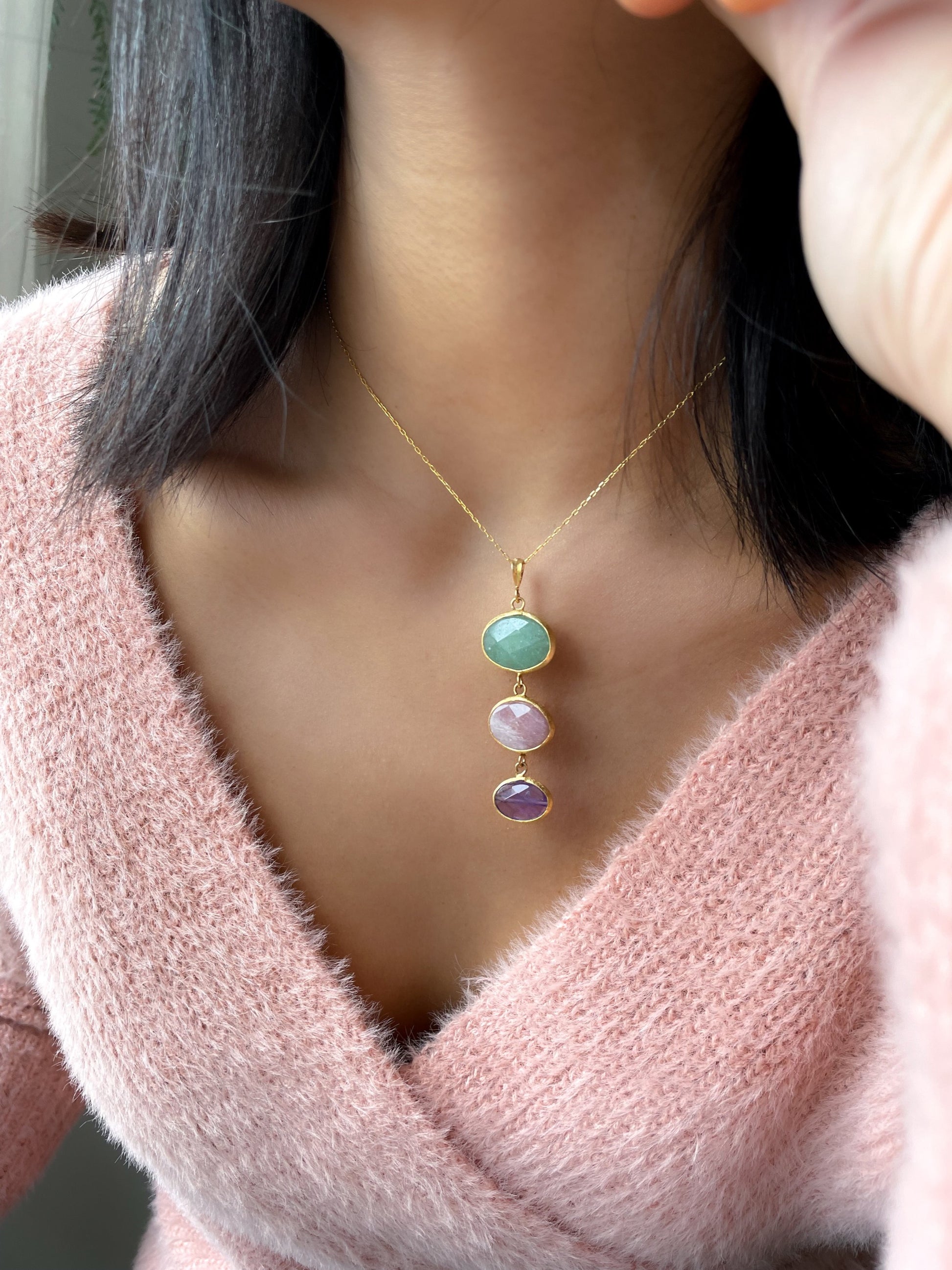 woman with a pink cardigan wearing Three graces necklace, green aventurine, pink moonstone, amethyst pendant