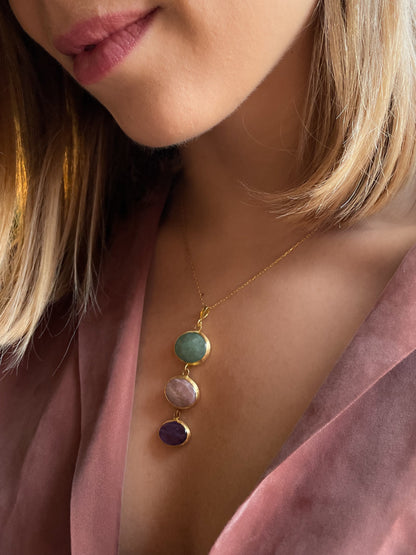 Close up of a woman with a pink shirt wearing Charites necklace, green aventurine, pink moonstone, amethyst pendant.