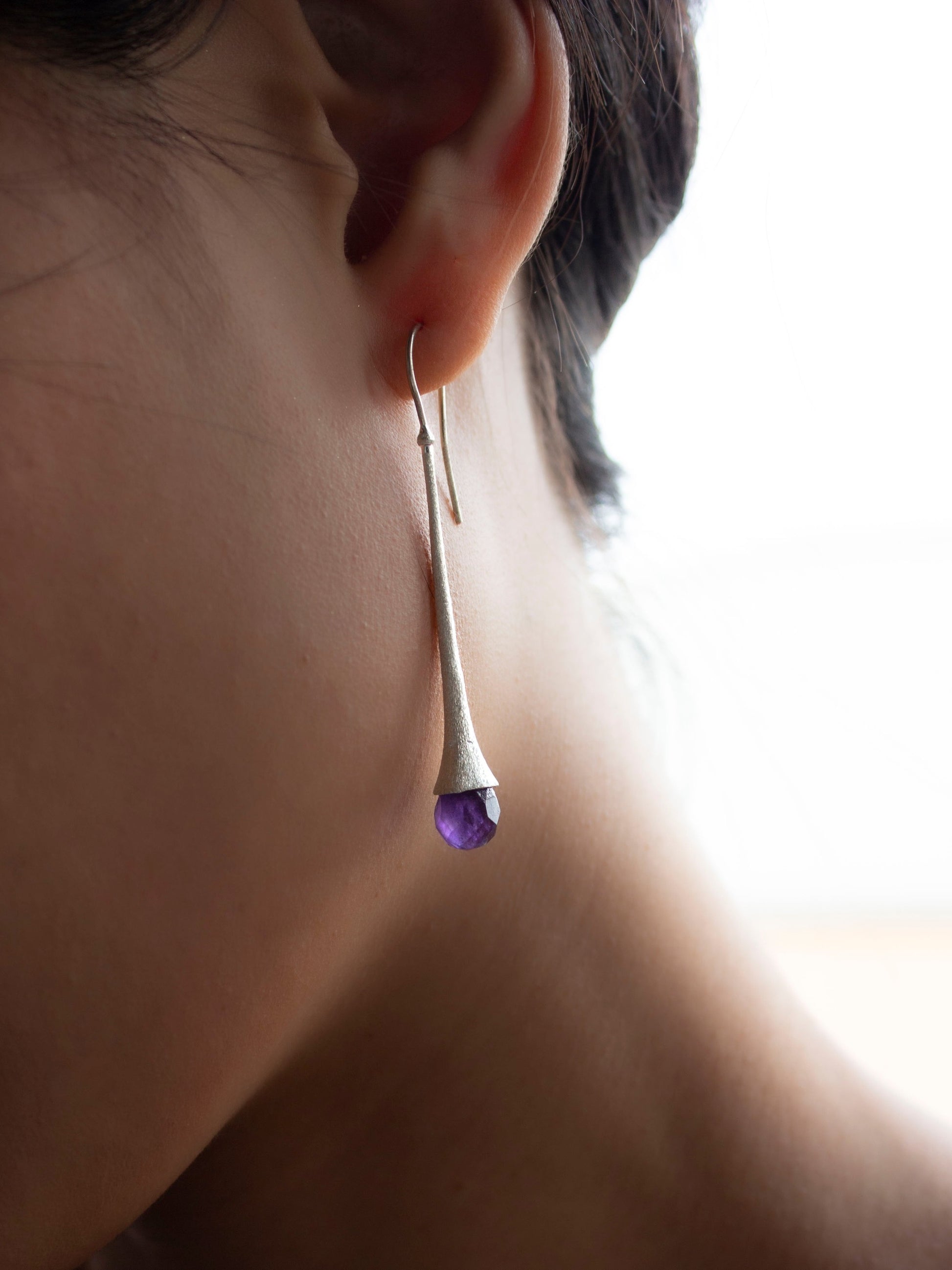 Girl wearing a long and chic silver earring with a briolette cut amethyst gemstone