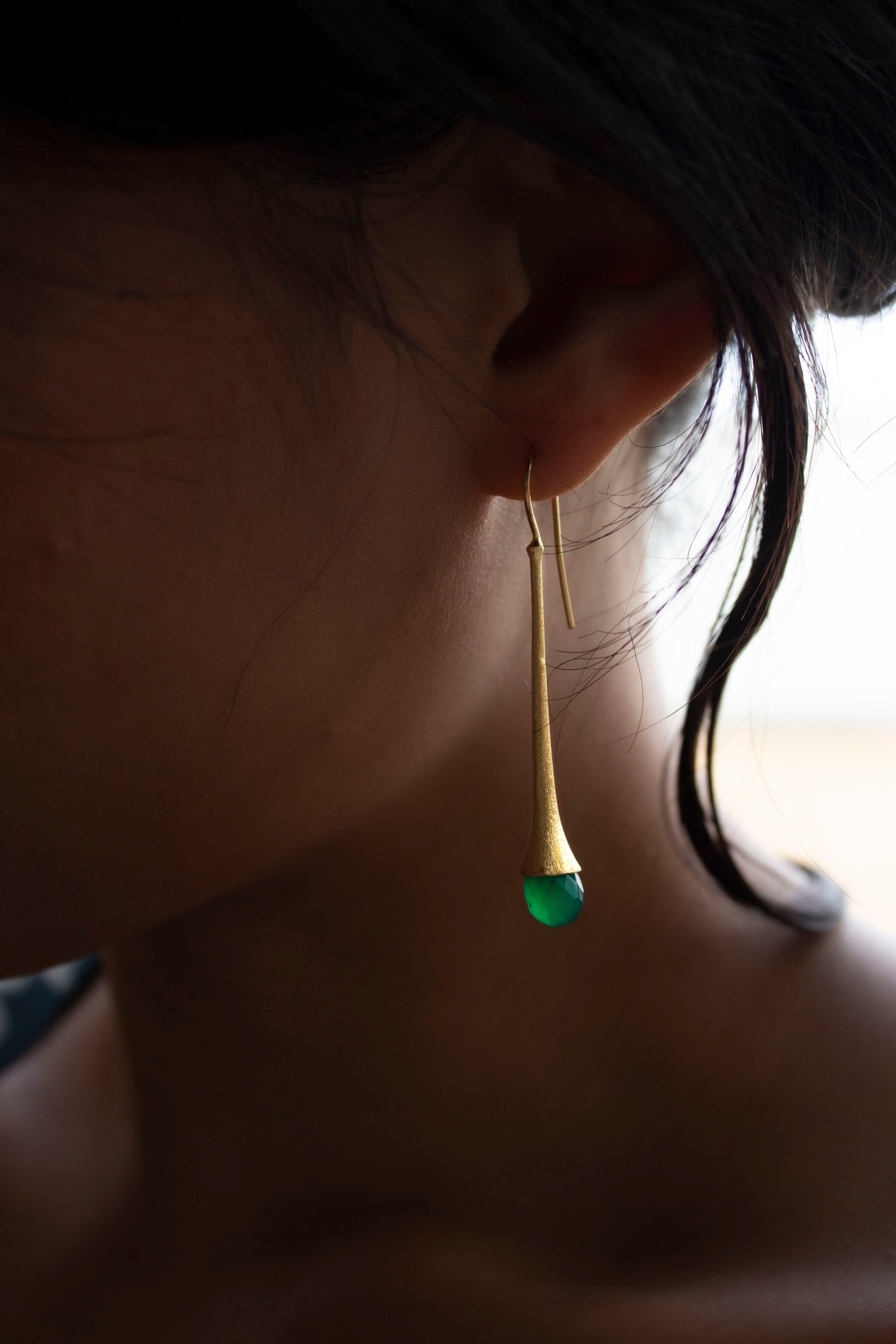 Girl wearing a long and chic gold earring with a briolette cut jade gemstone