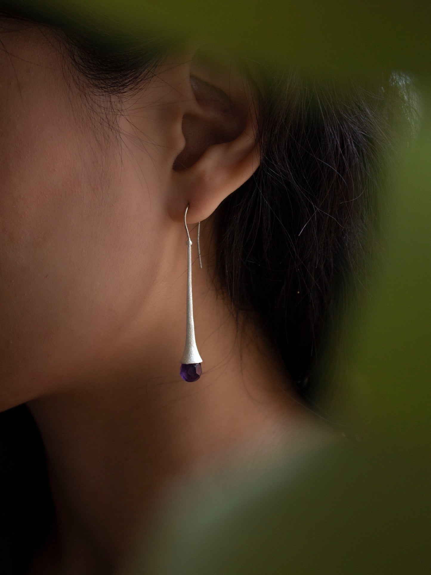 A brunette girls wearing a handmade lean and chic sterling silver earring completed with a shiny amethyst gemstone