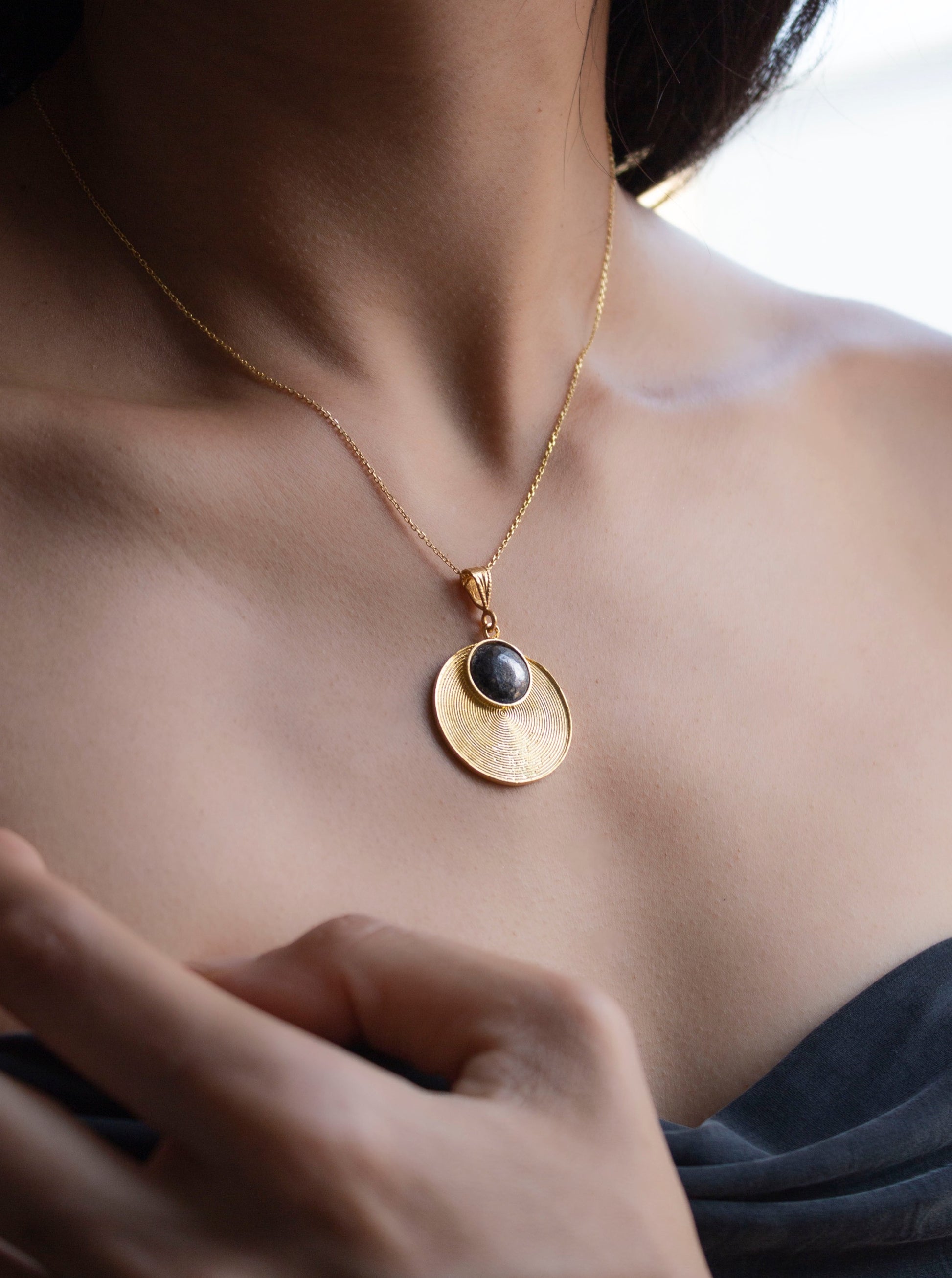 Girl wearing eclisse necklace, gold pendant with spiral forms and a circle oxidised piece