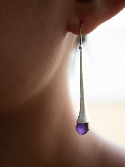 Girl wearing a long and chic silver earring with a briolette cut amethyst gemstone  Edit alt text
