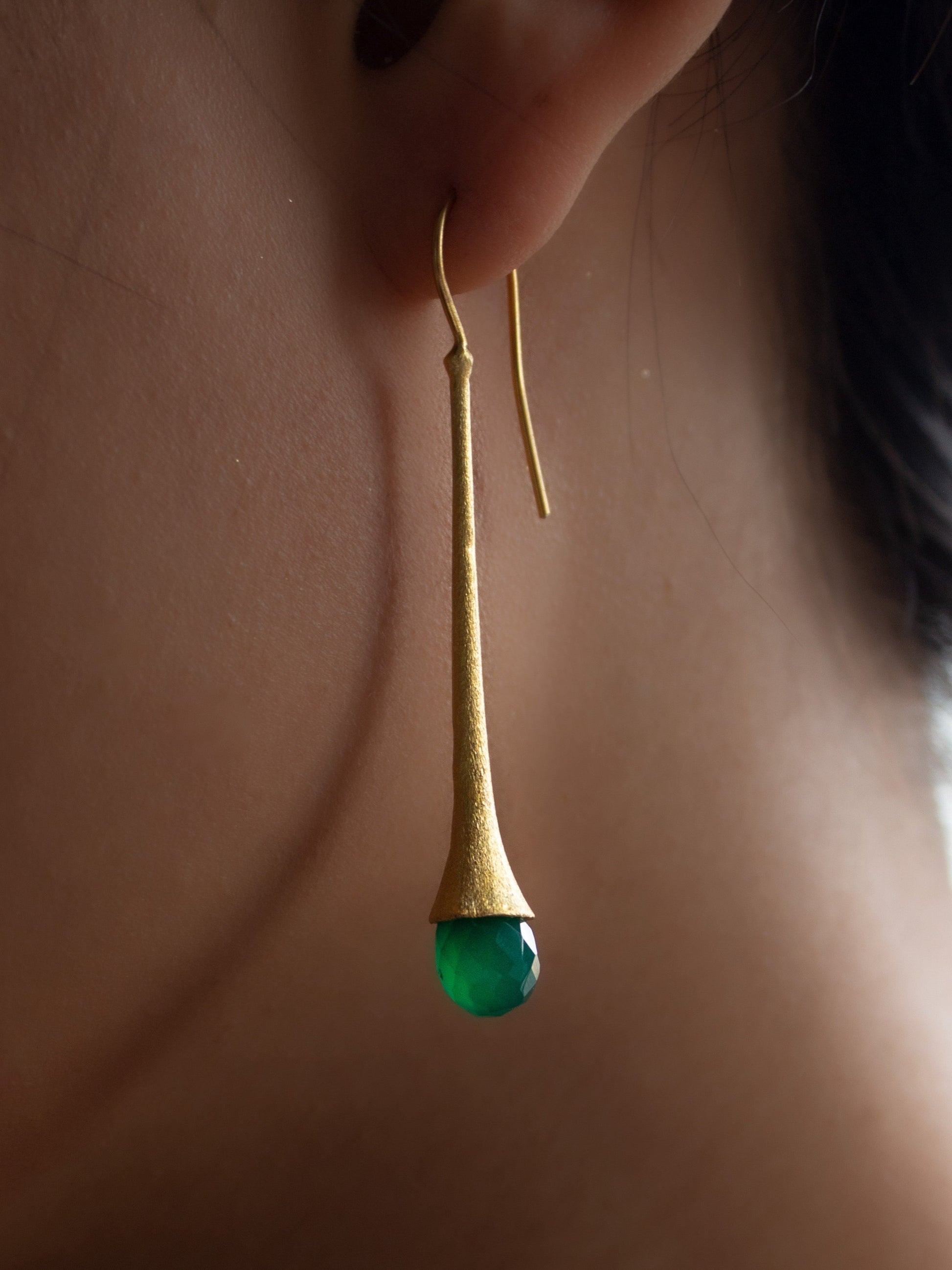 Girl wearing a long and chic gold earring with a briolette cut jade gemstone